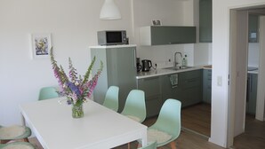 A modern kitchen with a white countertop, green cabinets, and a microwave. There is a dining area with a white table and green chairs, and a vase with flowers on the table. - Renovated, bright, light-flooded 4-room apartment (Saig)