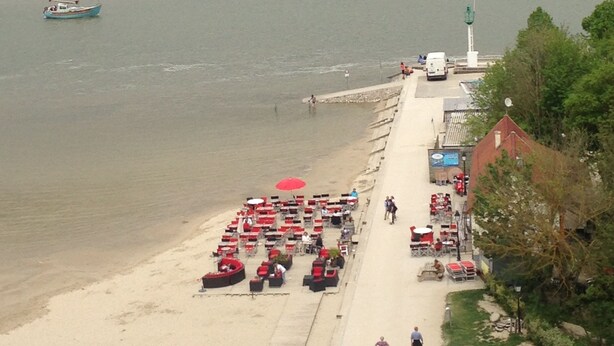 A coastal area with a sandy beach, a row of red umbrellas, and a few people walking.