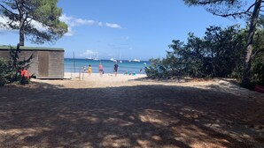 Une plage avec une structure en bois, un ciel dégagé et des bateaux à l’horizon.