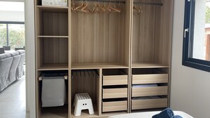 Un dressing avec des étagères en bois, une tringle pour suspendre les vêtements et un petit tabouret.