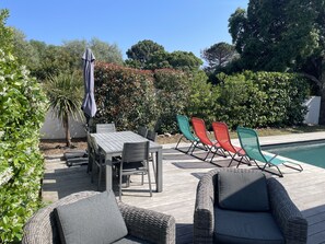 Een terras buiten met een zwembad, rieten meubels en een tafel met stoelen.