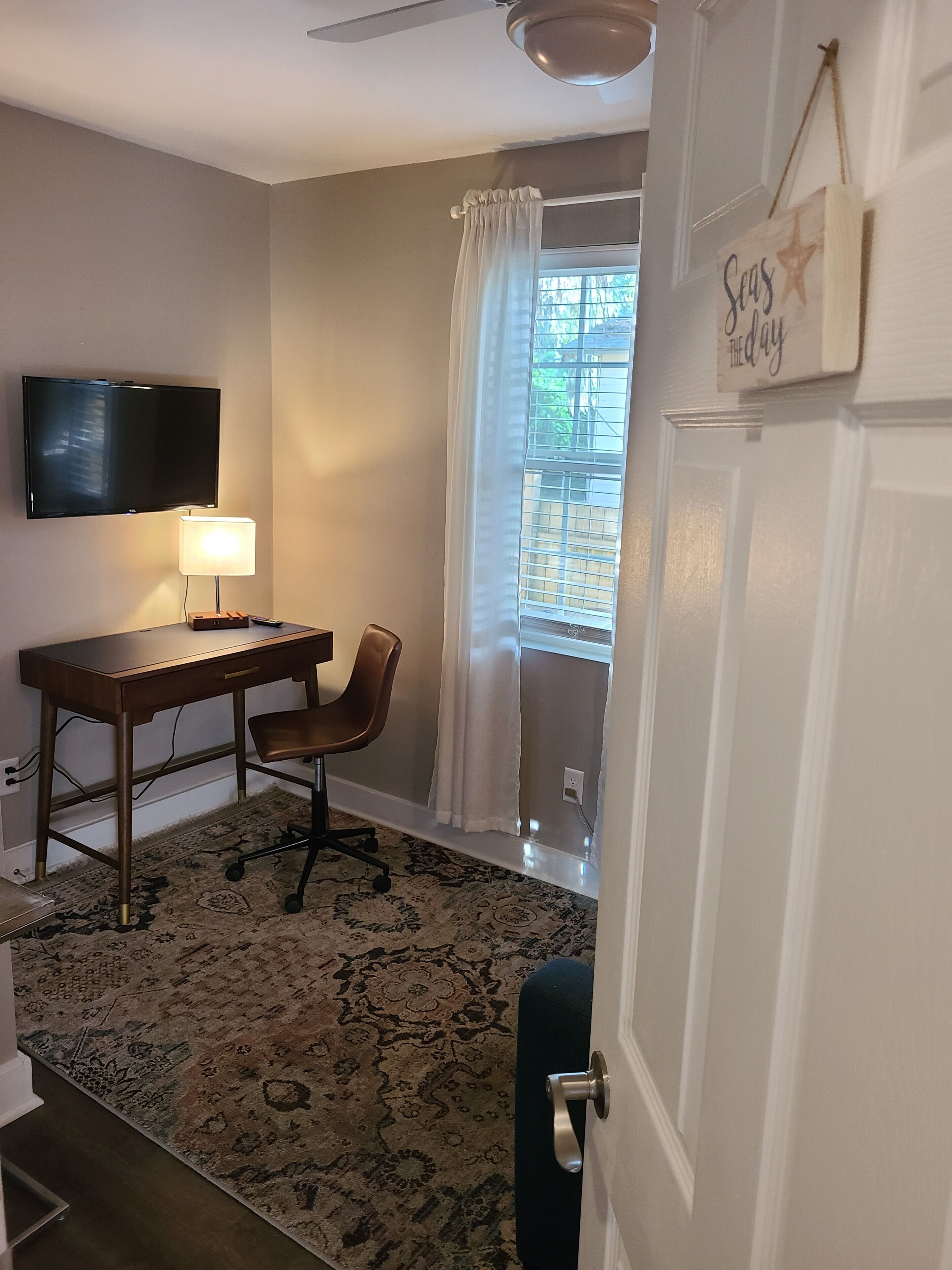 Una habitación con escritorio, silla, televisor y ventana con cortinas.