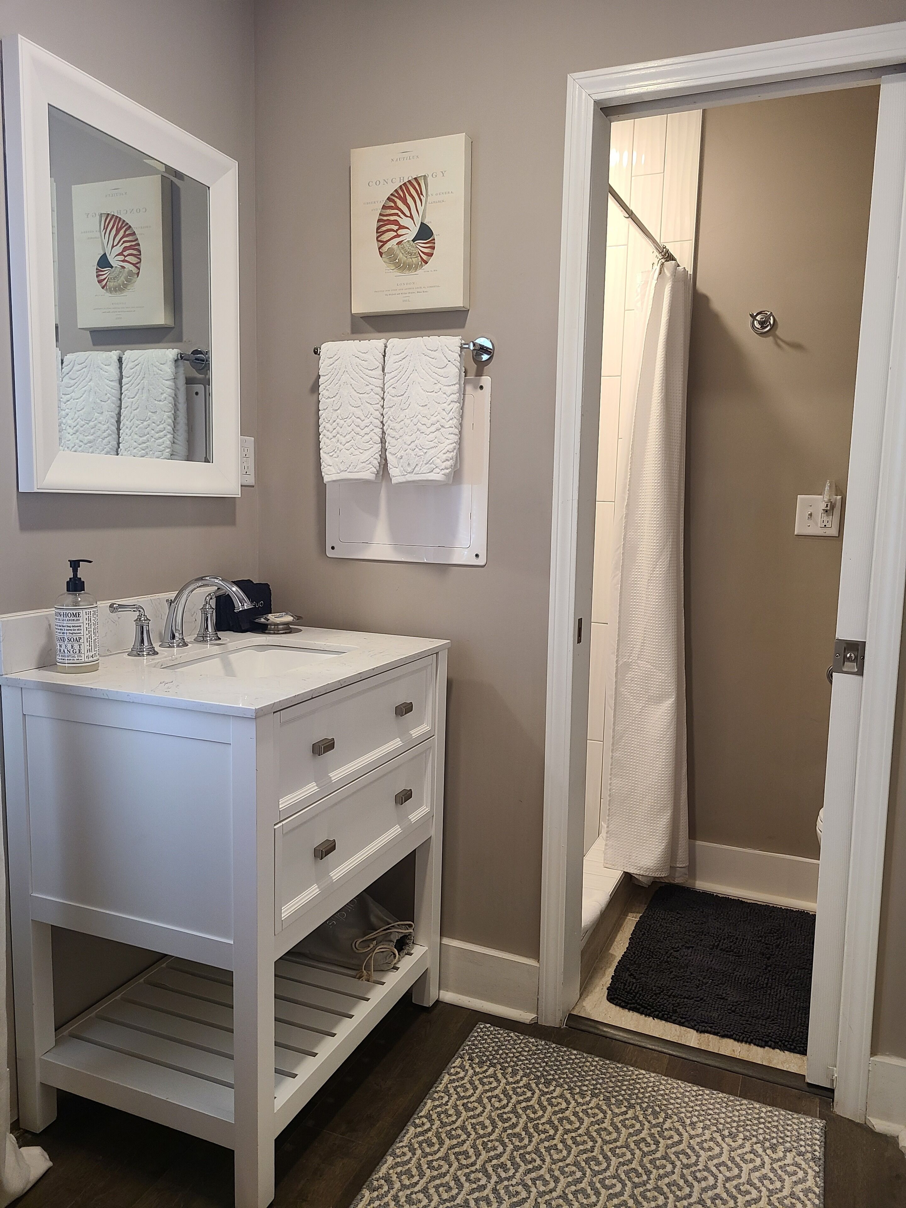 A bathroom with a white vanity, a mirror, a towel rack with two towels, a shower curtain, and a patterned rug.