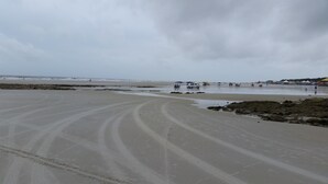 Een strand met een zandstrand, enkele rotsen en een paar mensen.