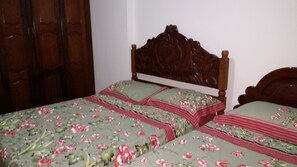 A bed with a floral bedspread and matching pillows, a wooden headboard, and a wooden door in the background.