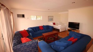 A living room with blue sofas, a white sofa, a television, and a small table.