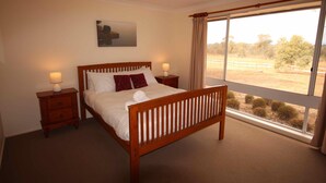 A bedroom with a wooden bed, two bedside tables with lamps, a window with curtains, and a painting on the wall.