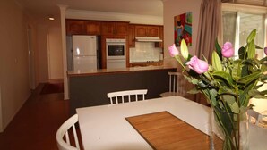 A dining area with a table, chairs, a vase with flowers, and a kitchen in the background.