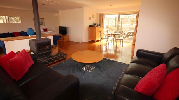 A living room with a fireplace, a black leather sofa, a round coffee table, and a dining area with a table and chairs.