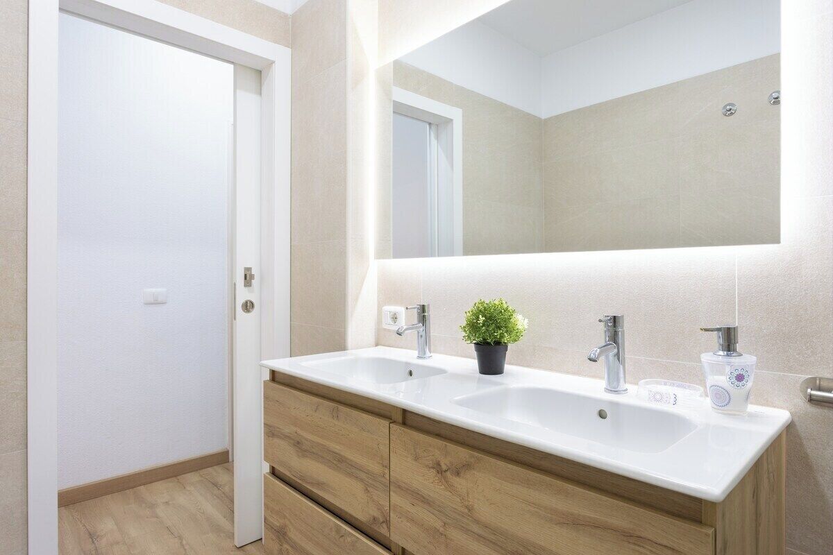 Un baño moderno con lavamanos doble, tocador de madera y un espejo grande.