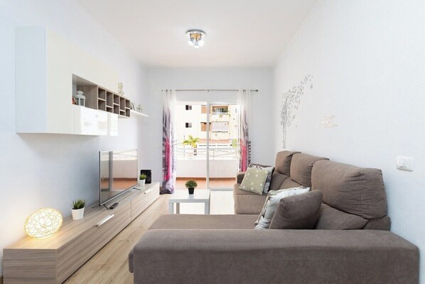 Una sala de estar moderna con un sofá, televisor y una pequeña mesa con una planta.
