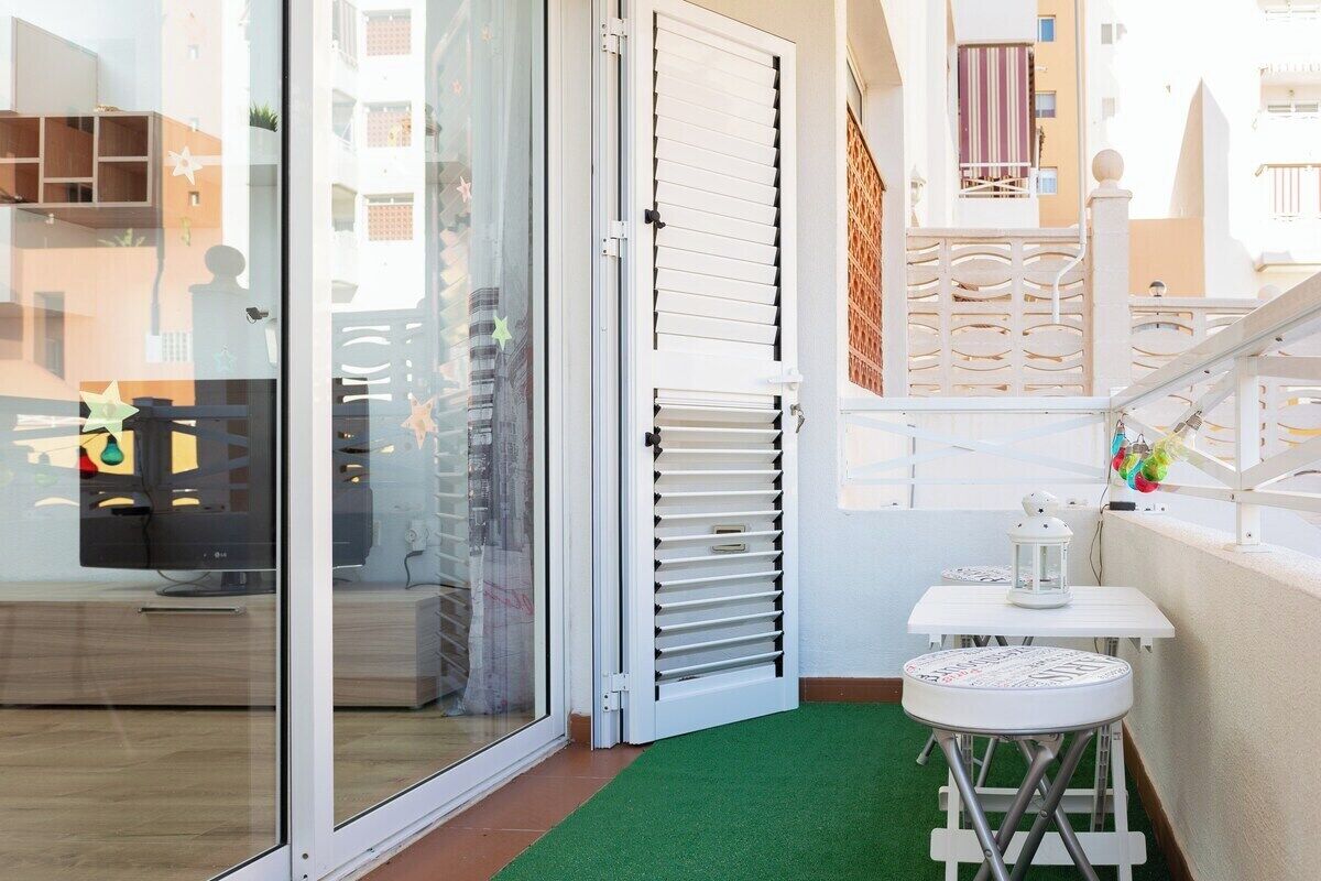A modern apartment with a sliding glass door, a small white table with a lantern, and a green artificial turf area.