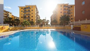 A swimming pool surrounded by yellow buildings with balconies, palm trees, and a lifebuoy on the wall. - Home2Book Charming Caletillas Pool (Candelaria)