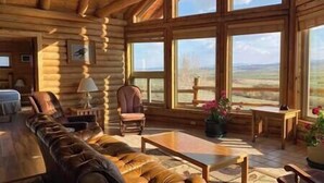 L’intérieur d’une cabane en rondins, avec une grande fenêtre, un canapé en cuir, une table en bois et une chaise.