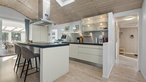 A modern kitchen with a central island, bar stools, and a view of the outdoors through large windows. - Nice home in Blåvand with sauna (Blåvand)