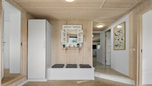 A hallway with wooden panel walls, a white bench with cushions, a decorative sign, and a framed wildlife illustration on the wall. - Nice home in Blåvand with sauna (Blåvand)