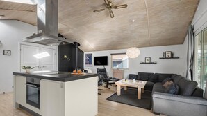 A modern kitchen with a central island, a dining area with a sofa and table, and a living room with a large window. - Nice home in Blåvand with sauna (Blåvand)