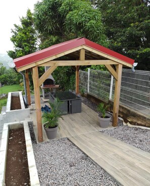 Une pergola en bois avec un toit rouge, un espace barbecue et des plantes en pot.