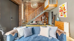 Un salon avec un canapé bleu, un escalier en bois et un mur en briques.