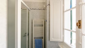 Casa de banho com chuveiro, um porta-toalhas e uma janela com porta.