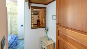 Um corredor com uma porta de madeira, um espelho com moldura ornamentada, uma mesa pequena com um vaso e um edredom estampado.