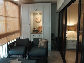 Una habitación acogedora con dos sofás de mimbre, un mueble pequeño con objetos decorativos y una puerta corredera que da a otra habitación.