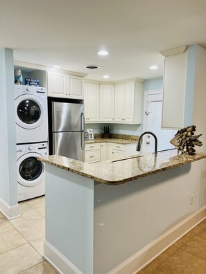 A modern kitchen with white cabinets, a stainless steel refrigerator, a built-in washing machine, and a granite countertop. - Best Queens Grant location: easy walk to all amenities. (Hilton Head Island)