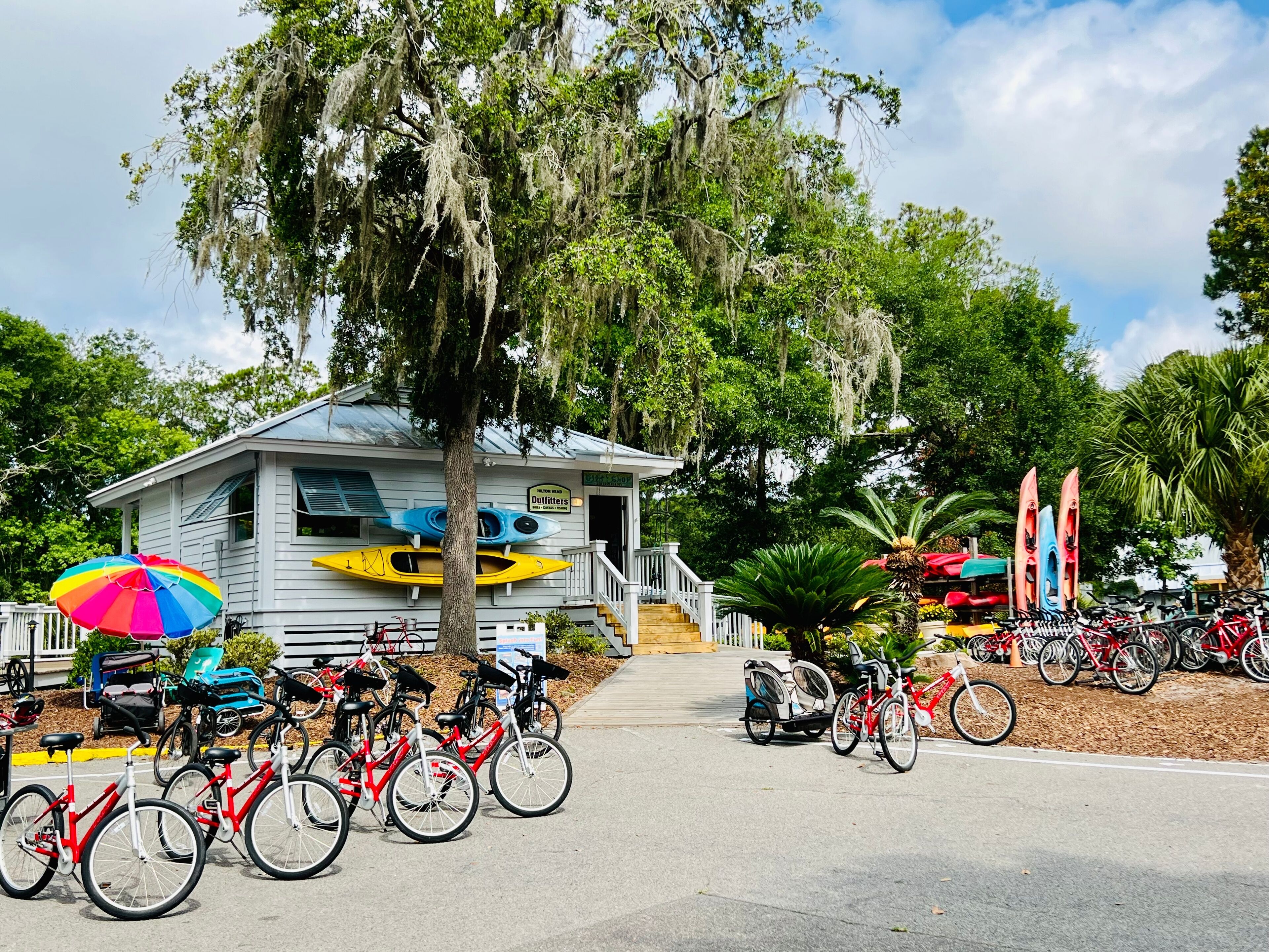 A small building with a porch, bicycles, kayaks, and a colorful umbrella.