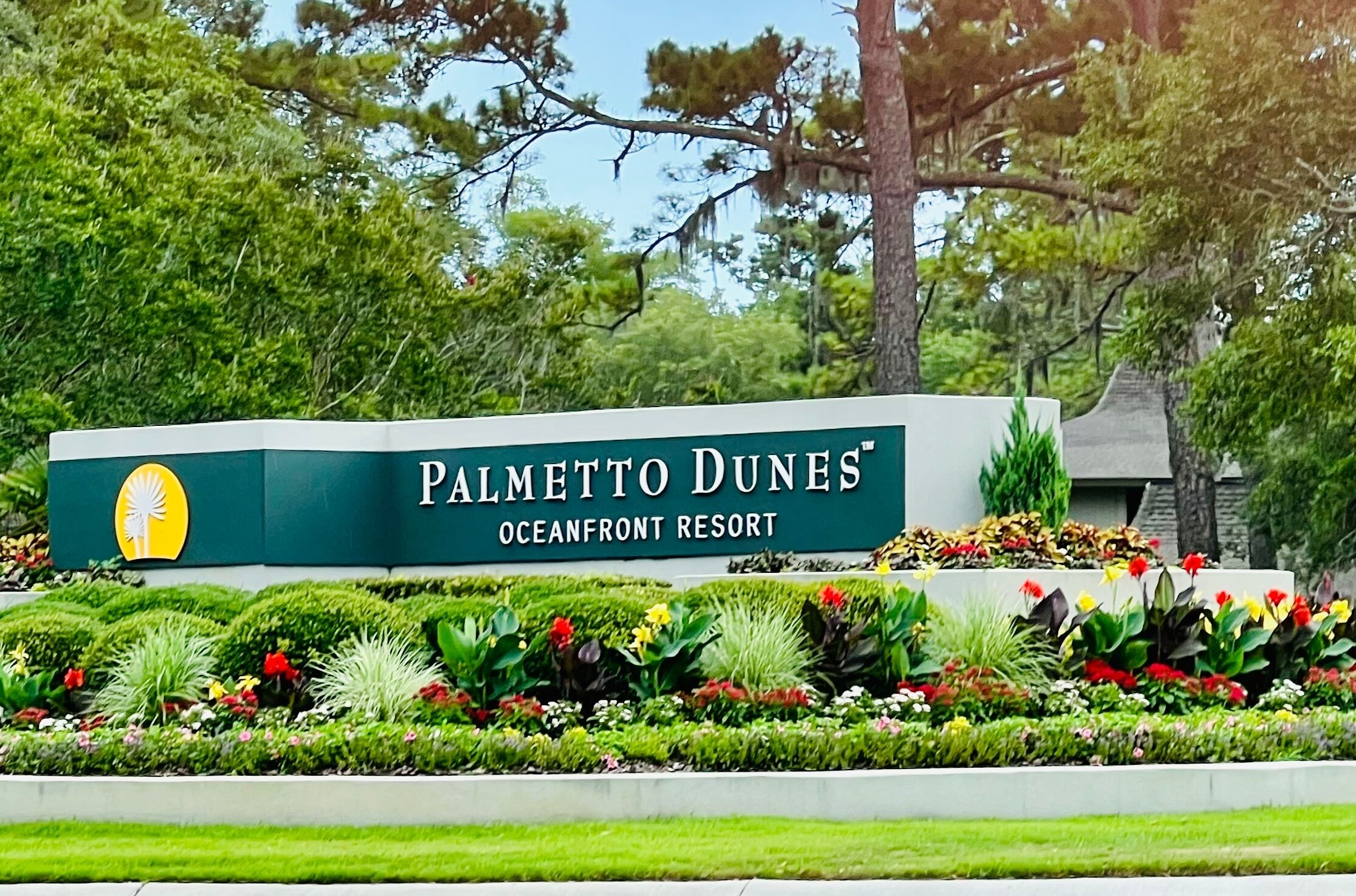 A sign for Palmetto Dunes Oceanfront Resort with a logo, surrounded by a landscaped garden with various plants and flowers.