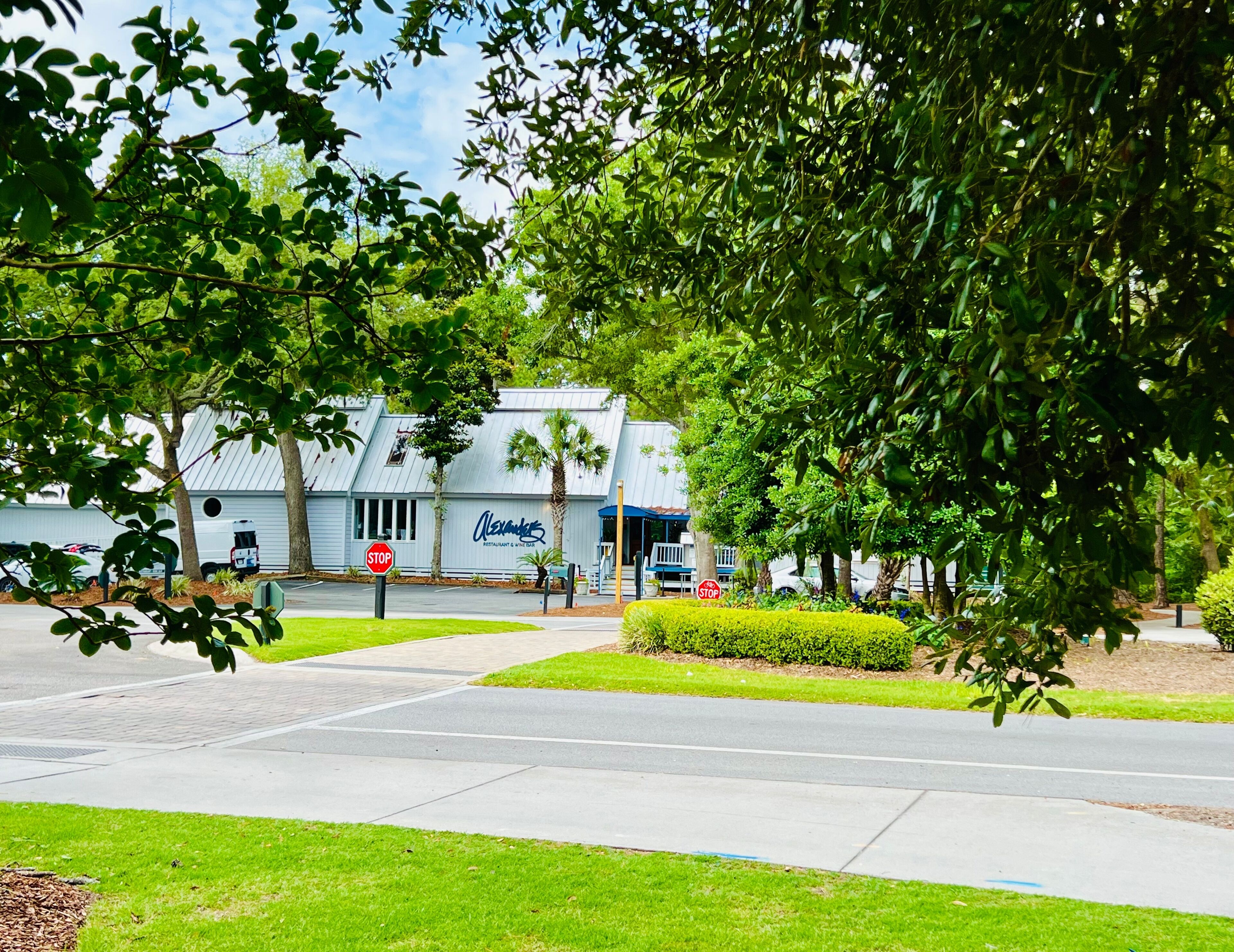A restaurant with a sign reading "Alexander's Restaurant & Bar" in a landscaped area with trees and a sidewalk.