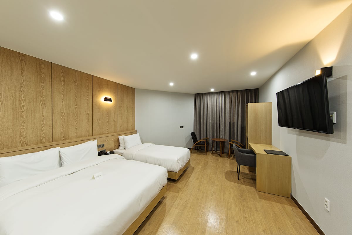 Habitación de hotel con dos camas, un escritorio, una silla, un televisor y una cortina.