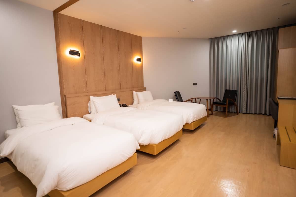 Habitación de hotel con dos camas individuales, cabecero de madera, una mesita, una silla y un armario.