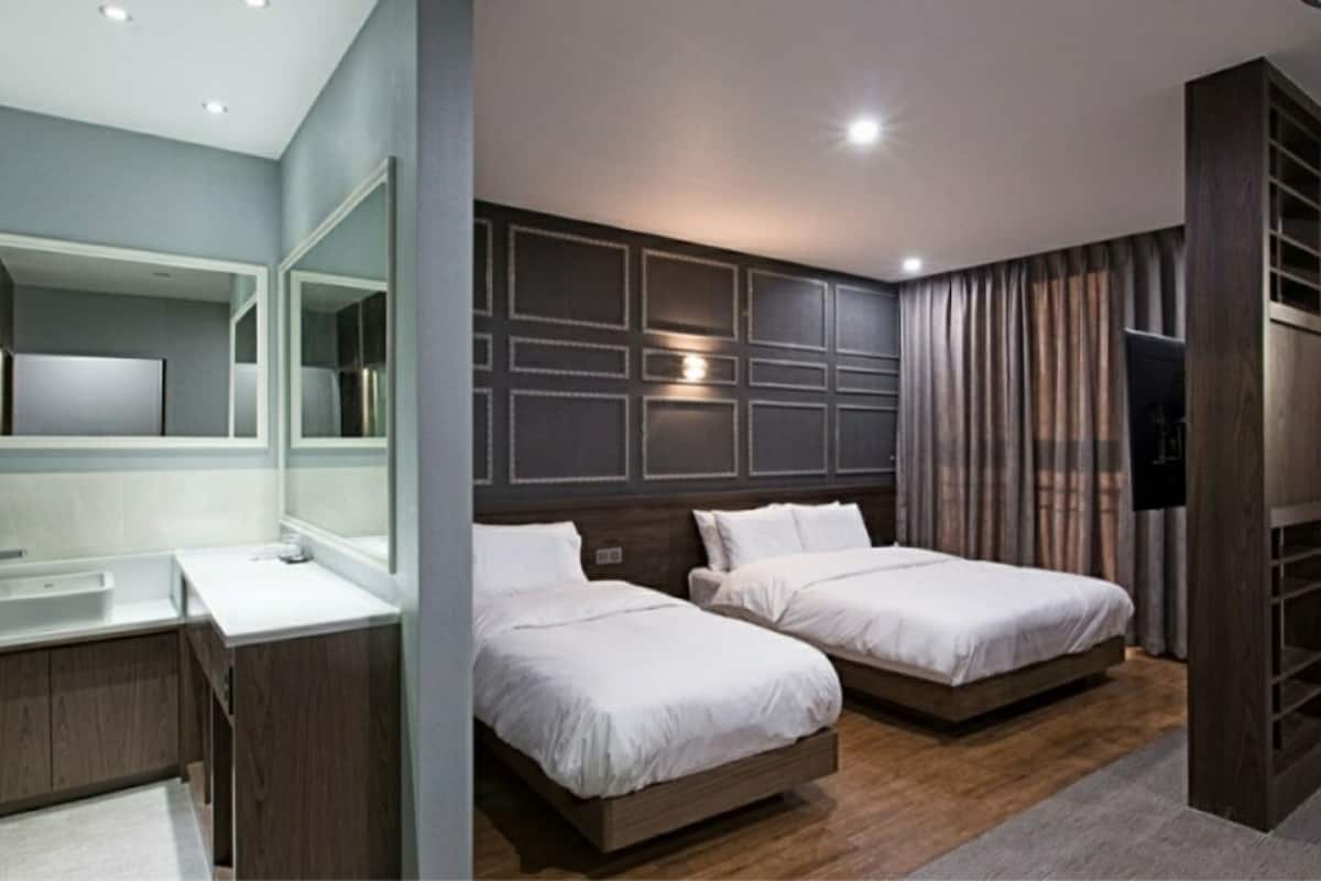 Una habitación de hotel moderna con un espejo grande, dos camas, piso de madera y una televisión.