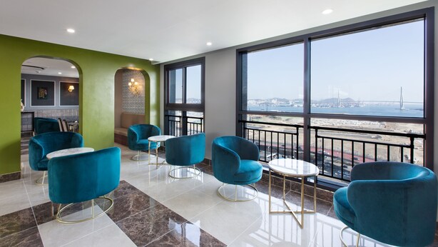 A modern lounge area with teal chairs and a view of the cityscape through large windows. - Notte La Mia (Busan)