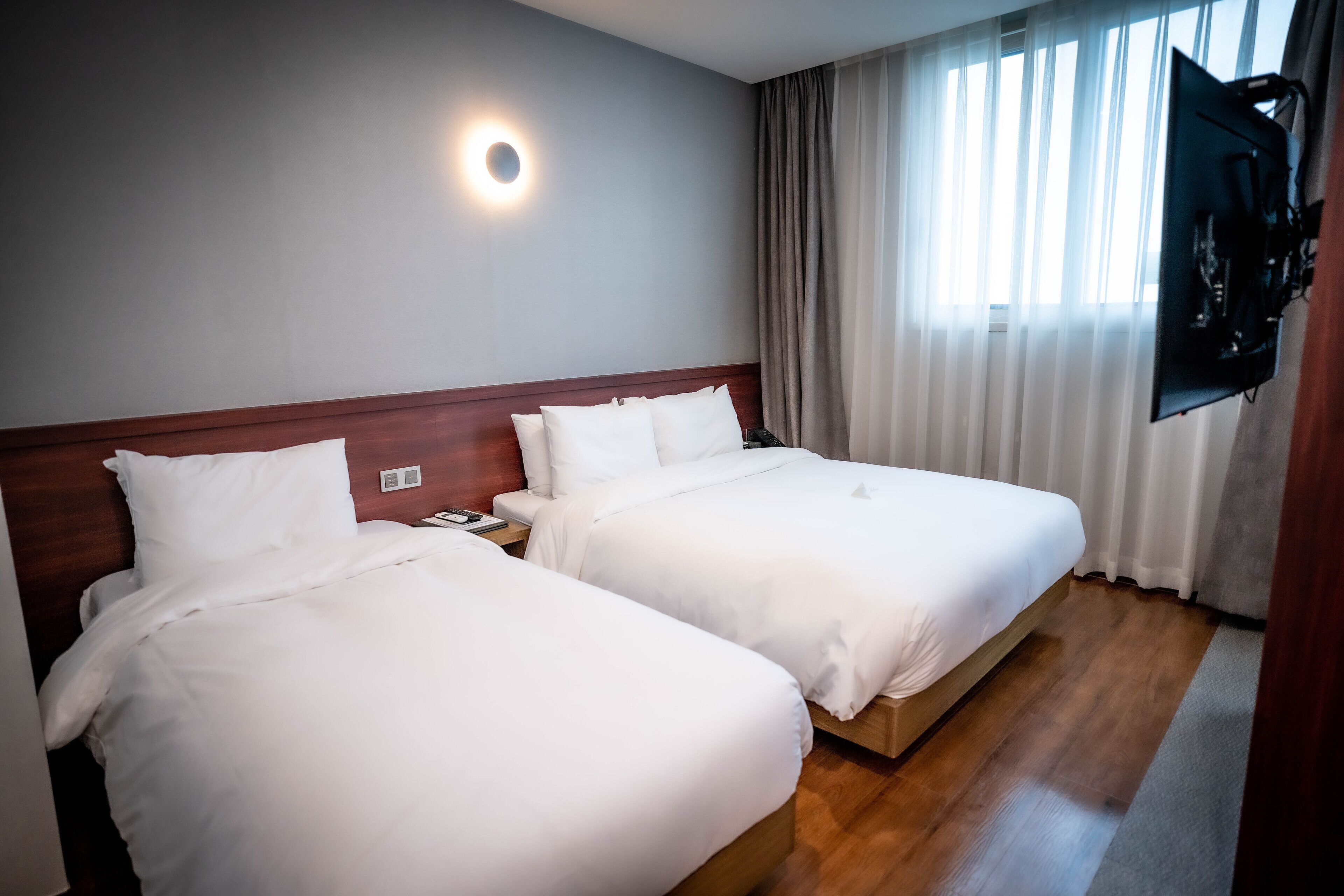A hotel room with two beds, a TV mounted on the wall, and a window with curtains.