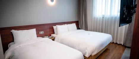 Habitación de hotel con dos camas, televisor montado en la pared y una ventana con cortinas.