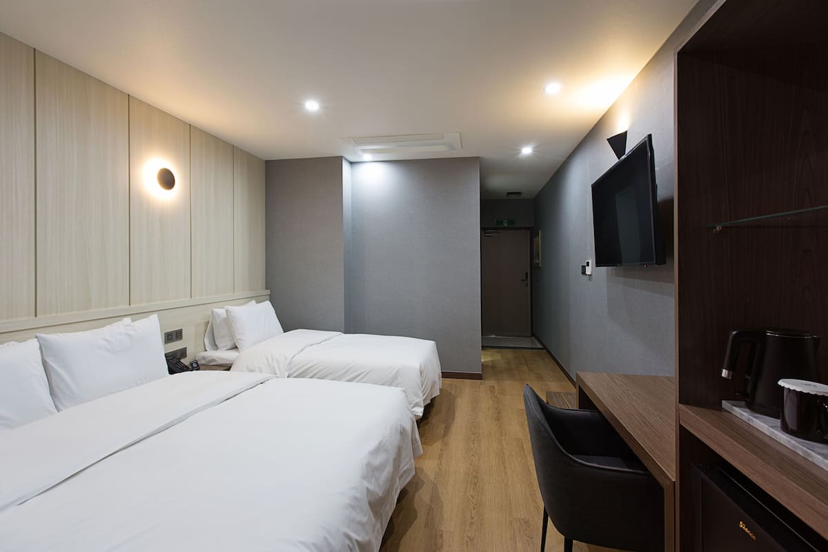 Habitación de hotel con dos camas, un escritorio, una silla, un televisor y una cafetera.