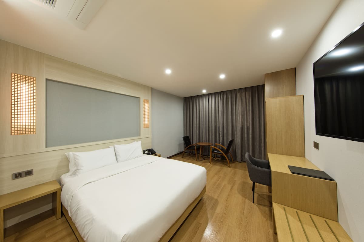 Una habitación de hotel moderna con una cama grande, un escritorio y una silla. Hay una pequeña mesa y un televisor montado en la pared.