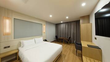 A modern hotel room with a large bed, a desk, and a chair. There is a small table and a TV mounted on the wall.