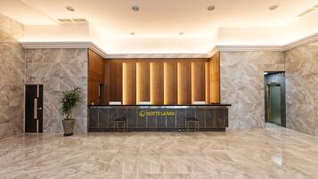 A hotel reception area with a marble floor, a reception desk, and a potted plant.
