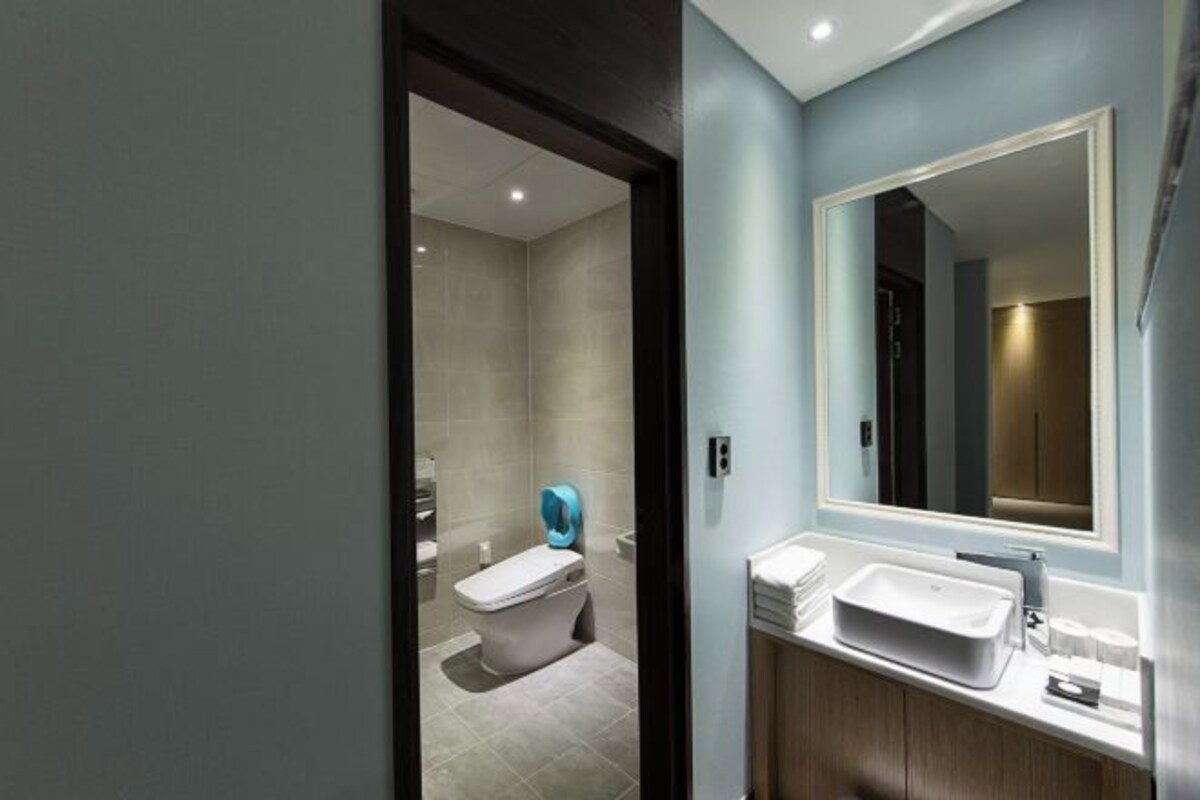 A modern bathroom with a large mirror, a white sink, and a toilet.