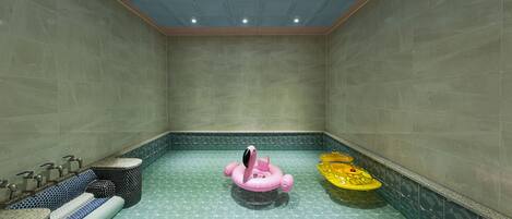 A spa area with a tiled floor, a pink and a yellow floating ring, and a seating area with a blue and black patterned bench.