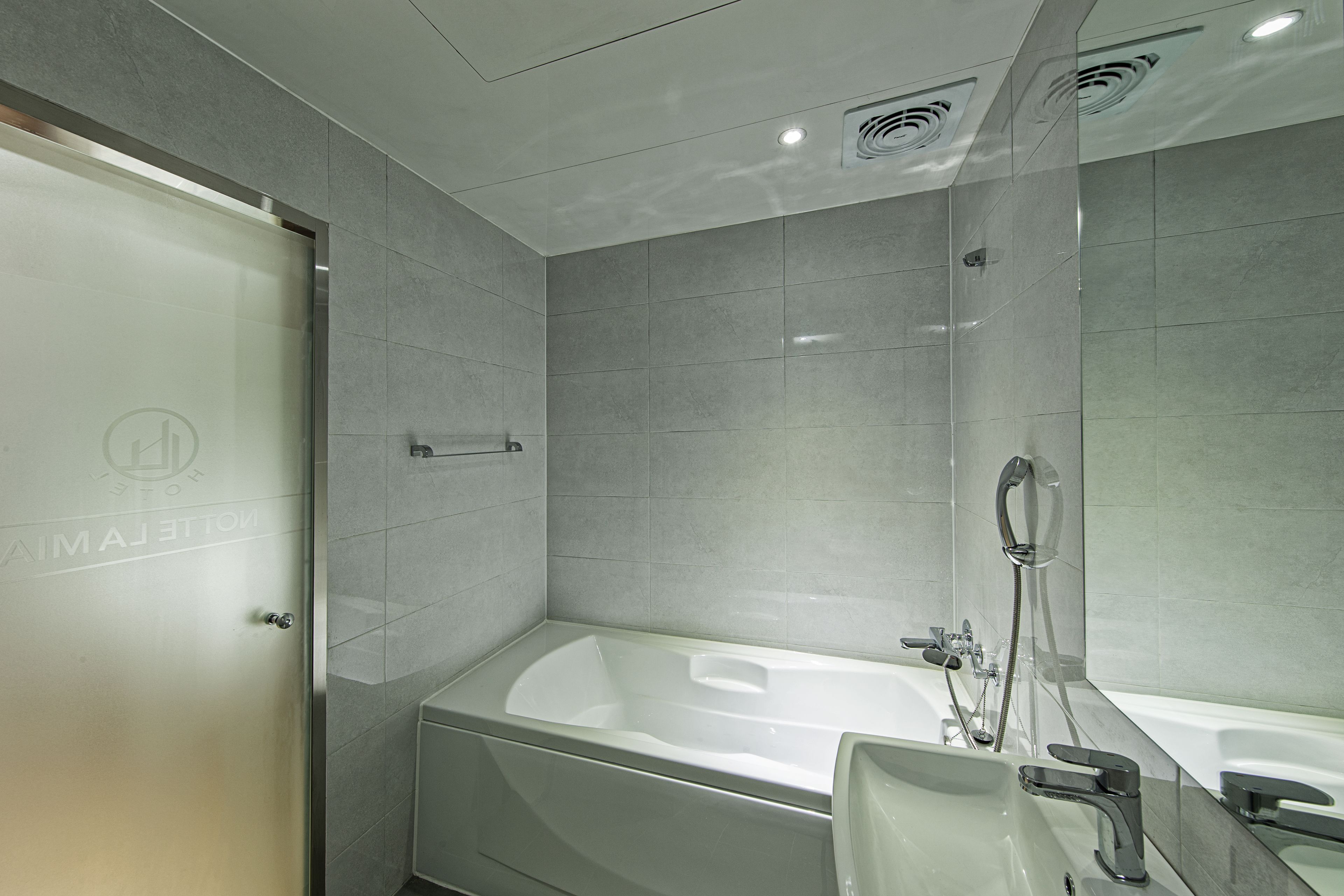 Een moderne badkamer met een groot bad, een aparte douche en een glazen deur met een logo.