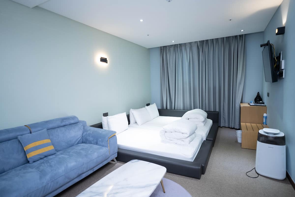 Una habitación de hotel moderna con cama, sofá, televisor de pantalla plana y una pequeña mesa.