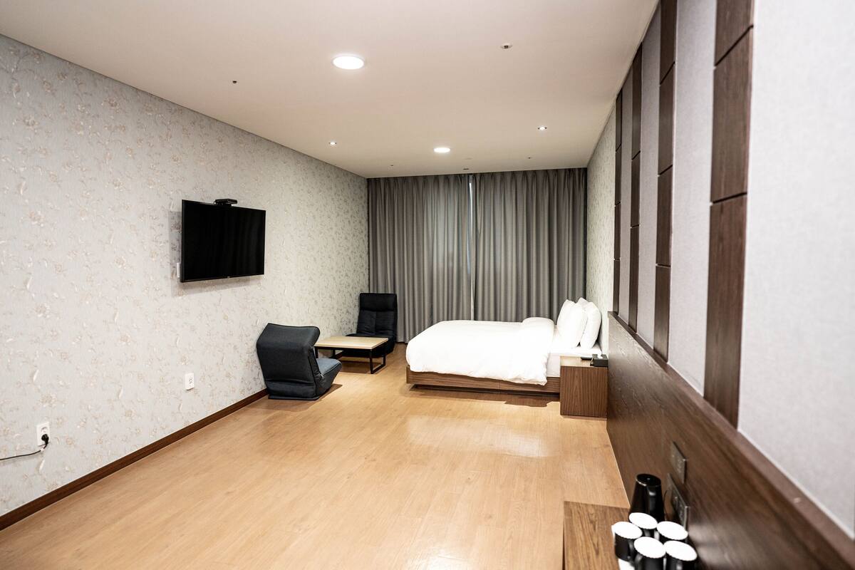 Habitación de hotel con cama, escritorio, silla, televisor y ventana con cortinas.