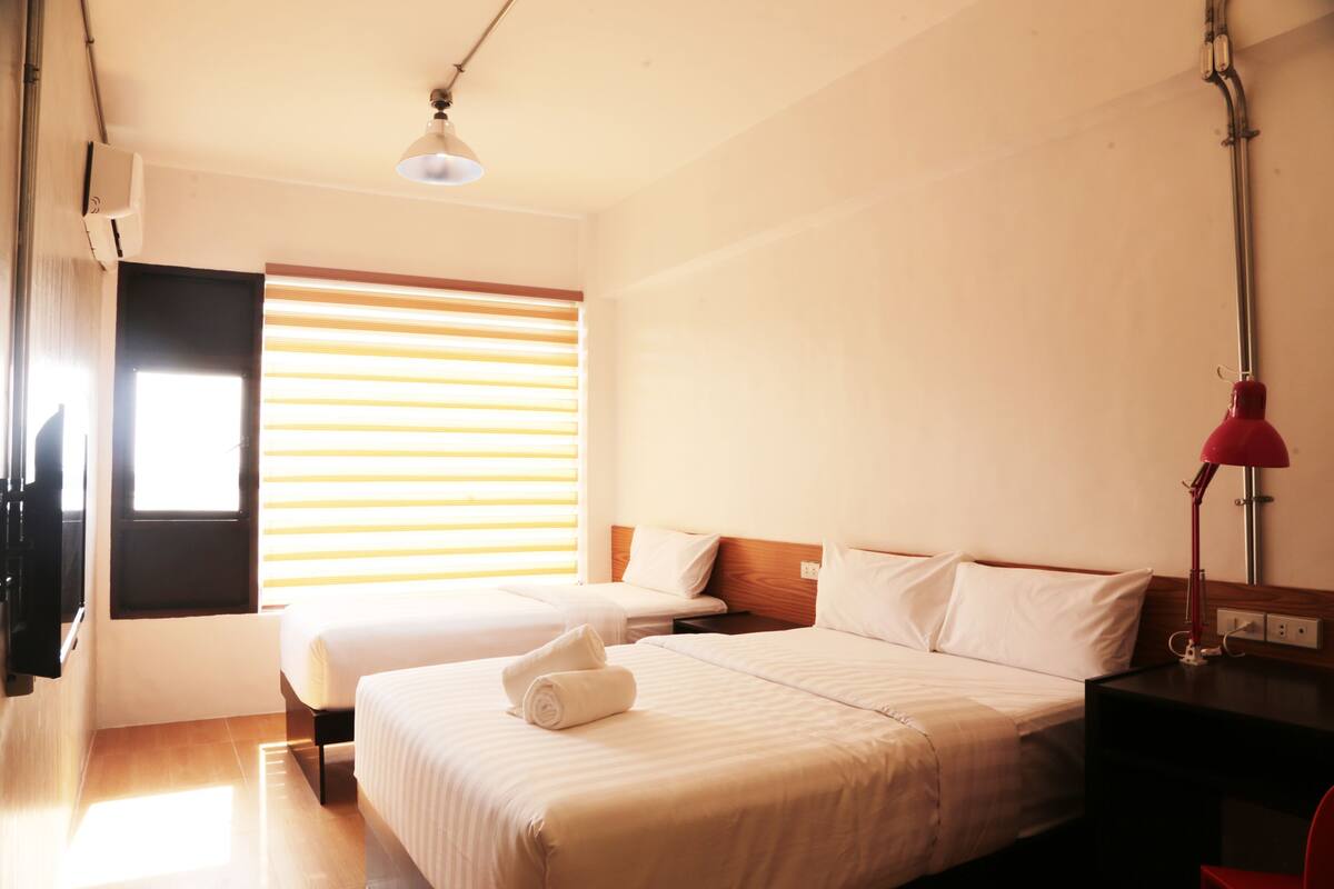 A hotel room with two beds, a desk, a lamp, and a window with blinds.