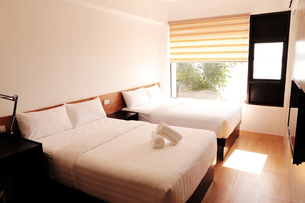 A hotel room with two beds, a nightstand, a lamp, and a window with blinds.