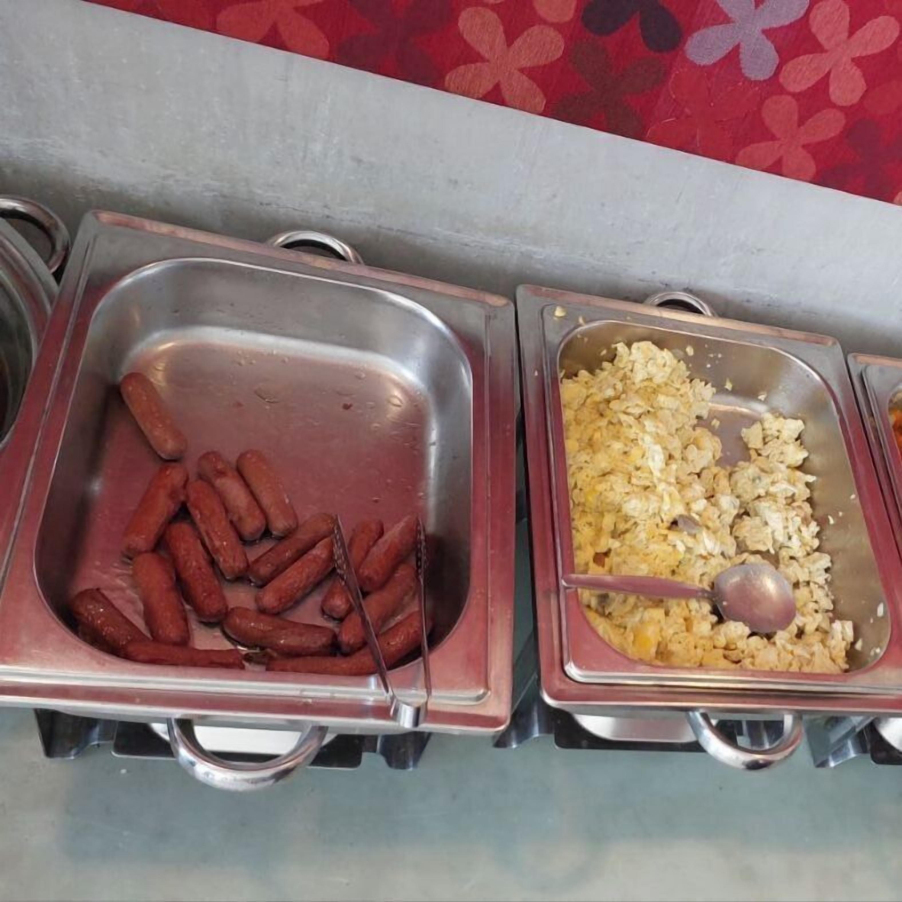 A buffet with two stainless steel serving trays, one containing sausages and the other containing scrambled eggs.