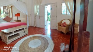 Ein Zimmer mit einem Bett, einem Sessel, einem kleinen Tisch und einer Tür, die nach draußen führt.