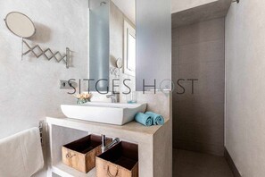 Une salle de bain moderne avec un lavabo blanc, un miroir et un porte-serviettes. On trouve deux paniers en bois sous le lavabo.